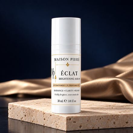 ÉCLAT brightening serum, 30 mL, on ivory stone with champagne fabric and a midnight-blue background