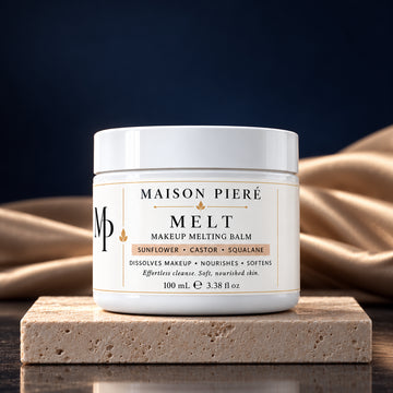 MELT makeup melting balm, 100 mL, on ivory stone with champagne fabric and a midnight-blue background