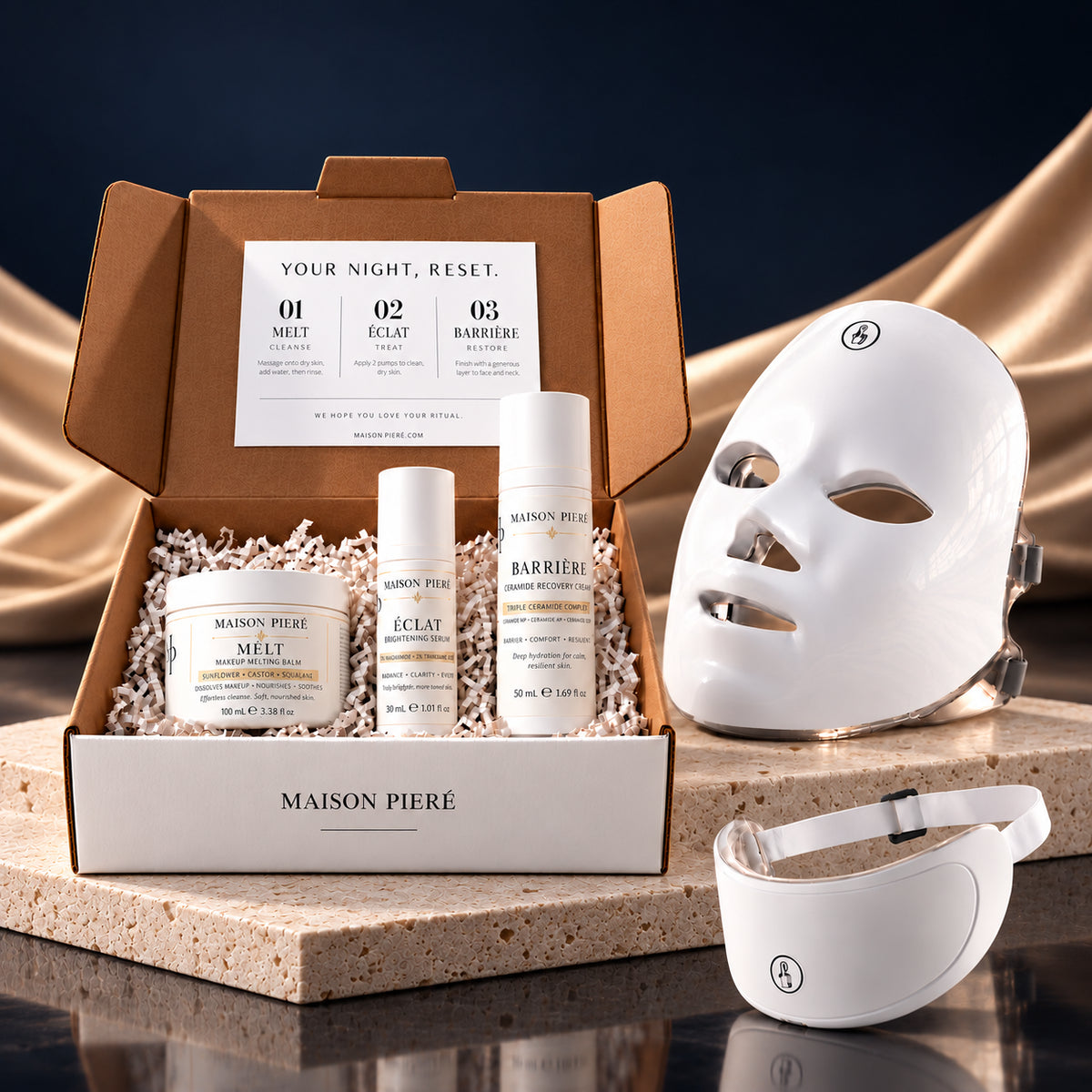 The Night Reset skincare box with LUMIÈRE face and neck mask, on ivory stone against midnight blue and champagne fabric