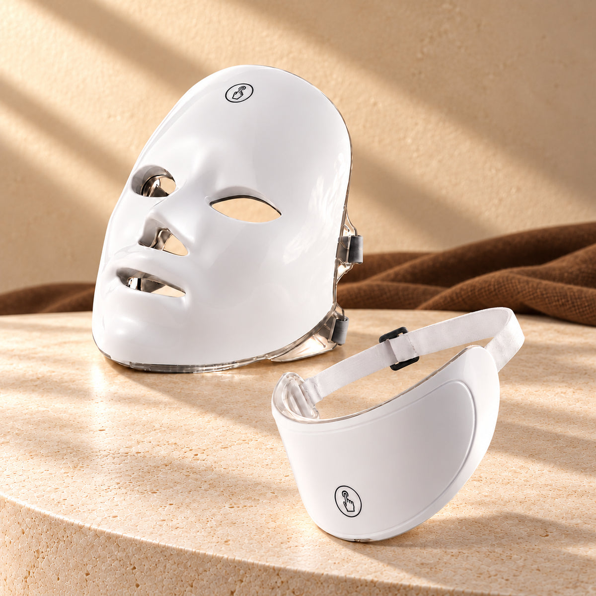 LUMIÈRE face mask and neck attachment with neutral-white packaging on ivory stone against champagne plaster and tobacco-brown linen